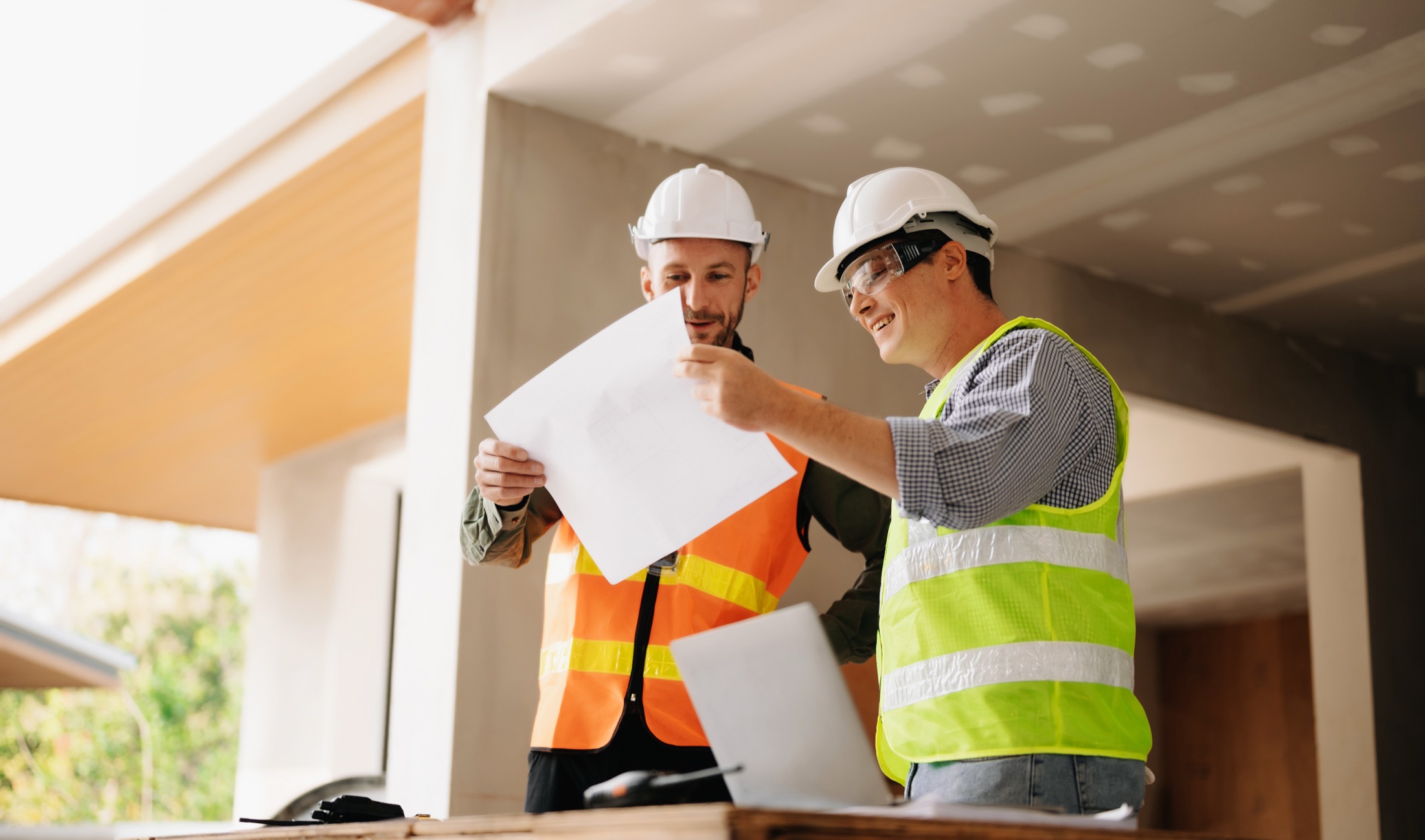 Two builders in hi-vis and hard hats reviewing plans together on a building site.