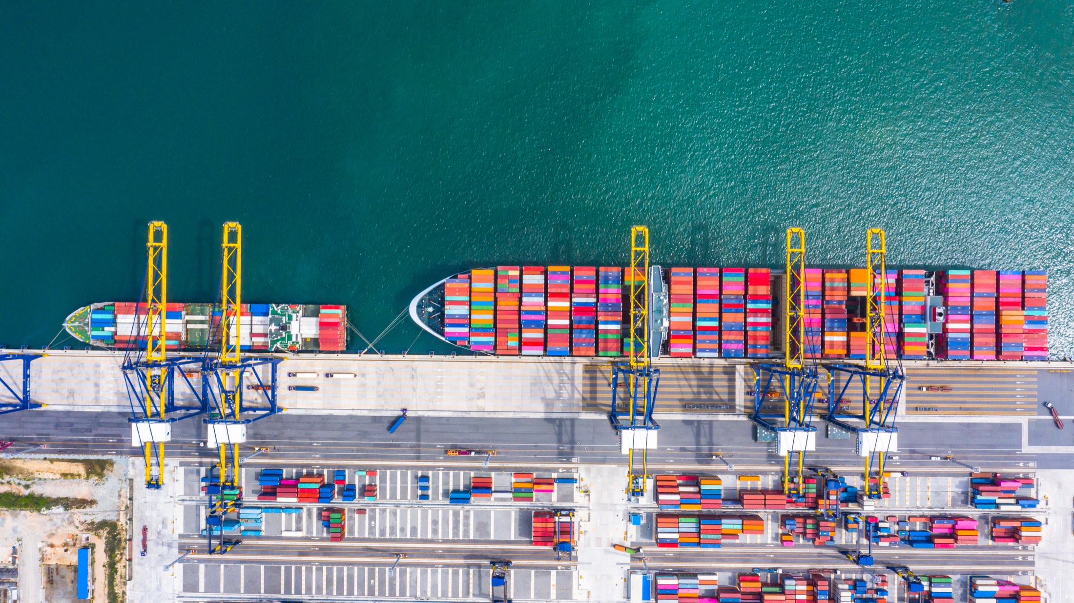 Aerial view of a container terminal, with container ships alongside the wharf and gantry cranes working.
