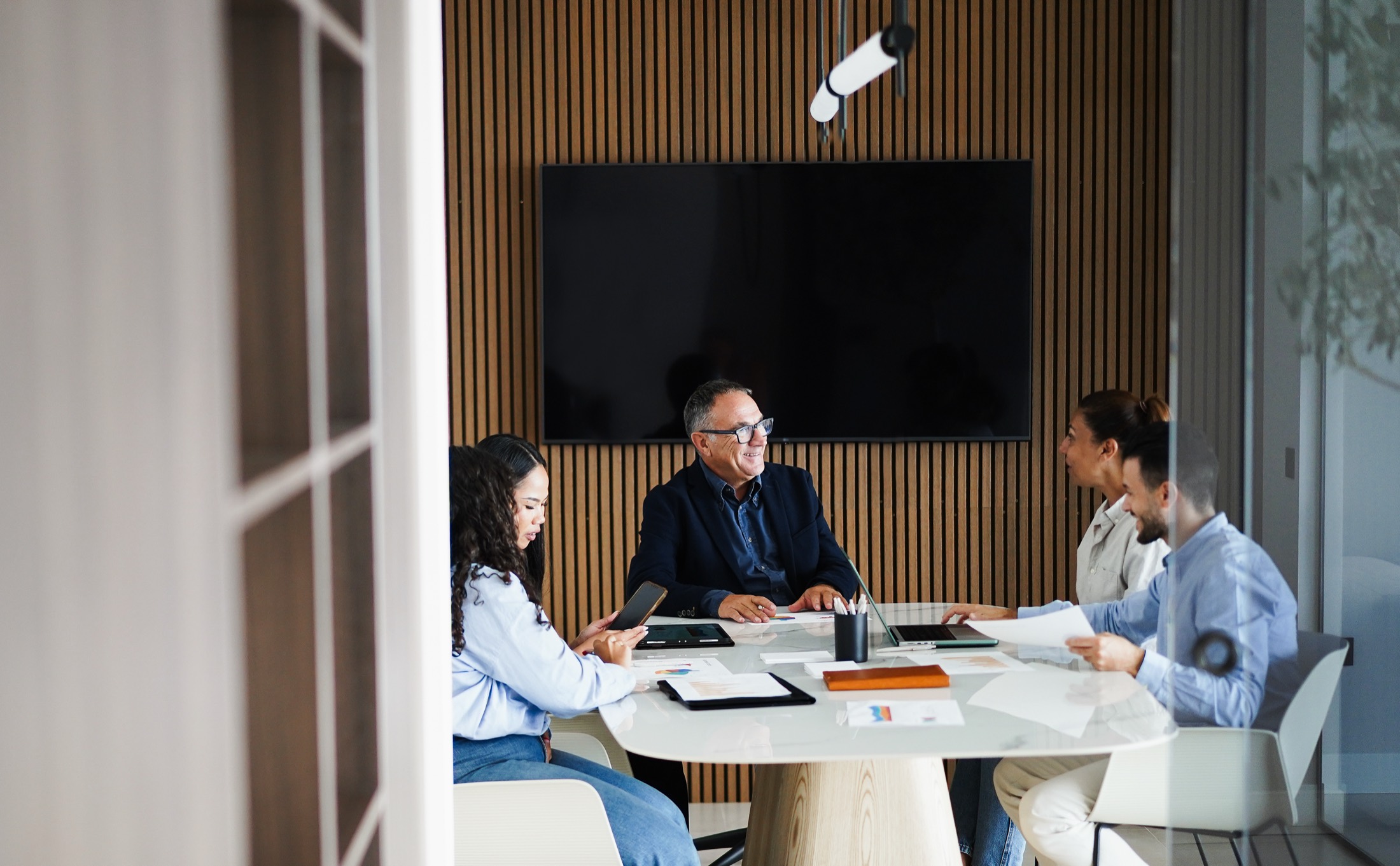 A group meeting around a boardroom table, working through printed documents together.