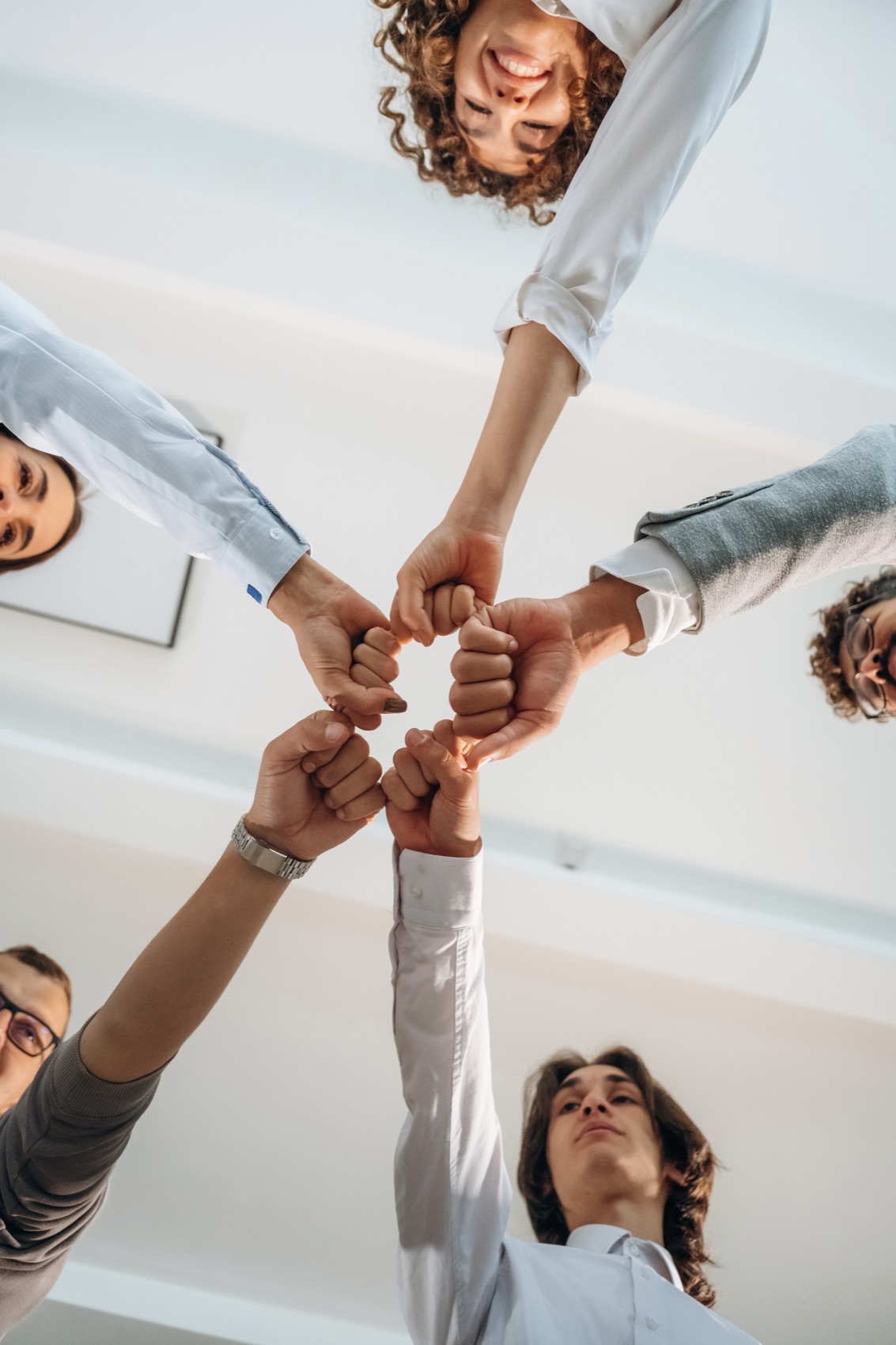 A team joining hands in a circle, photographed from below.