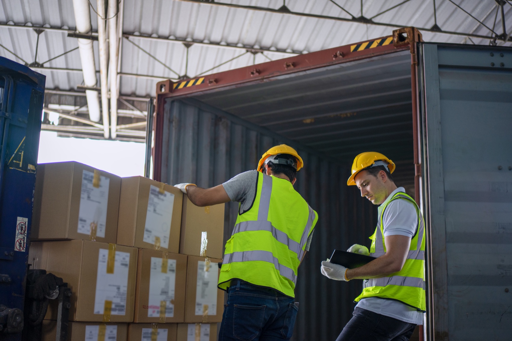 Two workers in hi-vis unloading cartons from a shipping container.